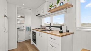 A modern kitchen with white cabinetry, a wooden countertop, and a window above the sink. - Husky Tiny Home by Experience Jervis Bay (Huskisson)