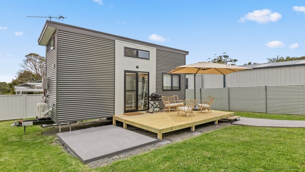 A modern single-story house with a covered patio area featuring outdoor furniture and a grill. - Husky Tiny Home by Experience Jervis Bay (Huskisson)