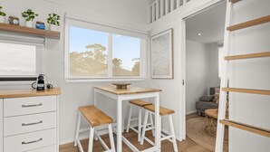 A compact kitchen with a window, a coffee machine, and a dining area with stools. - Husky Tiny Home by Experience Jervis Bay (Huskisson)