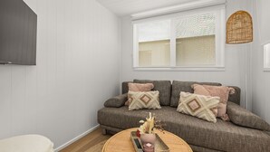 A living room with a grey sofa, two patterned throw pillows, a woven tray with a vase and candles, and a television mounted on the wall. - Husky Tiny Home by Experience Jervis Bay (Huskisson)