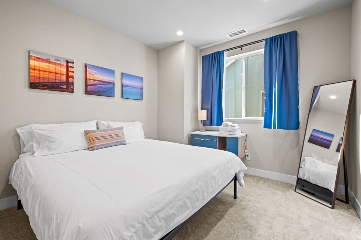 Ein Hotelzimmer mit einem großen Bett, einem Schreibtisch mit Stuhl, einem Spiegel und Bildern an der Wand.