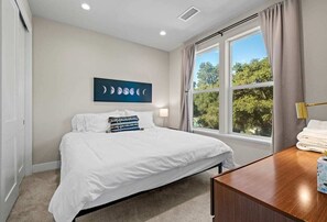 A bedroom with a bed, a bedside table, a window with curtains, and a wall-mounted artwork. - Serenity at the Russian River (Forestville)