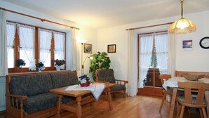 Ett mysigt vardagsrum med en soffa, fåtöljer, ett matbord och ett stort fönster med gardiner.