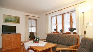 Ett vardagsrum med ett träskåp, en tv, en soffa och ett bord med en blomsteruppsättning.