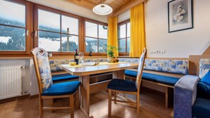 A room with a wooden table, blue cushioned chairs, a bench, a window with a view of a snowy landscape, and a framed picture on the wall. - Holiday Apartment "Niederkoflhof Wollbach" with Mountain View, Balcony & Wi-Fi (Valle Aurina)