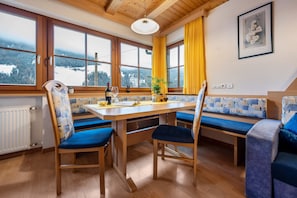 Una stanza con un tavolo in legno, sedie imbottite blu, una panca, una finestra con vista su un paesaggio innevato e un quadro appeso al muro.