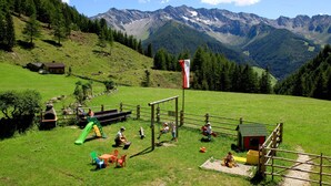 A playground with a slide, swings, and a climbing structure in a grassy field with mountains in the background.