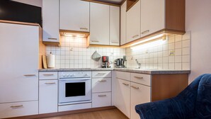 A compact kitchen with white cabinets, a built-in oven, a coffee maker, and a blue chair.
