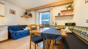 A cozy room with a dining table, chairs, a sofa, a blue couch, and a window with a view of a mountain.