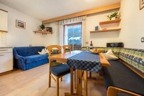 Une pièce chaleureuse comprenant une table à manger, des chaises, un canapé, un divan bleu et une fenêtre donnant sur une vue sur la montagne.