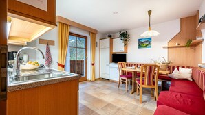 Una cucina con lavello, un tavolo da pranzo con sedie, un divano rosso e una televisione.