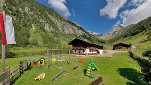 Un rifugio alpino con un'area giochi, cabine di legno e una vista panoramica sulle montagne circostanti.