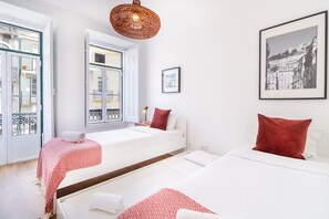 Habitación de hotel con dos camas, un ventanal grande, una lámpara colgante y una fotografía enmarcada de un paisaje urbano.