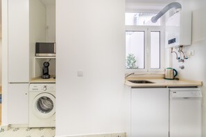 Uma cozinha compacta com máquina de lavar roupa, máquina de lavar louça e cafeteira na bancada.