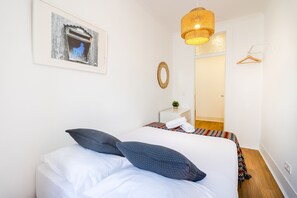 A bedroom with a bed, pillows, a hanging light fixture, a framed picture, a mirror, and a door.