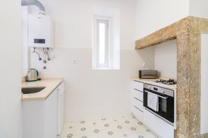 A compact kitchen with white cabinets, a built-in oven, a toaster, and a window. - Cozy Central Downtown II by Central Hill (Lisboa ciudad)