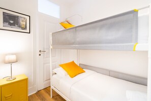 A bunk bed with a grey mattress and a yellow pillow, a white bedside table with a lamp, and a framed picture on the wall. - Cozy Central Downtown II by Central Hill (Lisboa ciudad)
