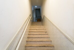 Uma escadaria com degraus de mármore e paredes brancas, que leva a um patamar.