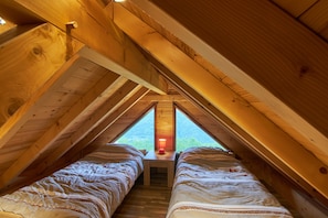 A wooden attic bedroom with two beds, a nightstand, and a window. - Chalet "La Traverse" with Mountain View, Whirlpool & Wi-Fi (Allemond)