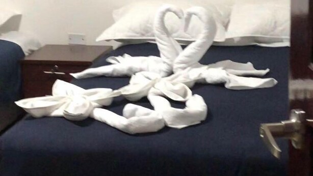 Habitación de hotel con una cama cubierta de toallas blancas dispuestas en forma de corazón.