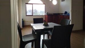 Un comedor con mesa y sillas, una ventana con vistas a edificios, y una zona de cocina con armarios y estufa.