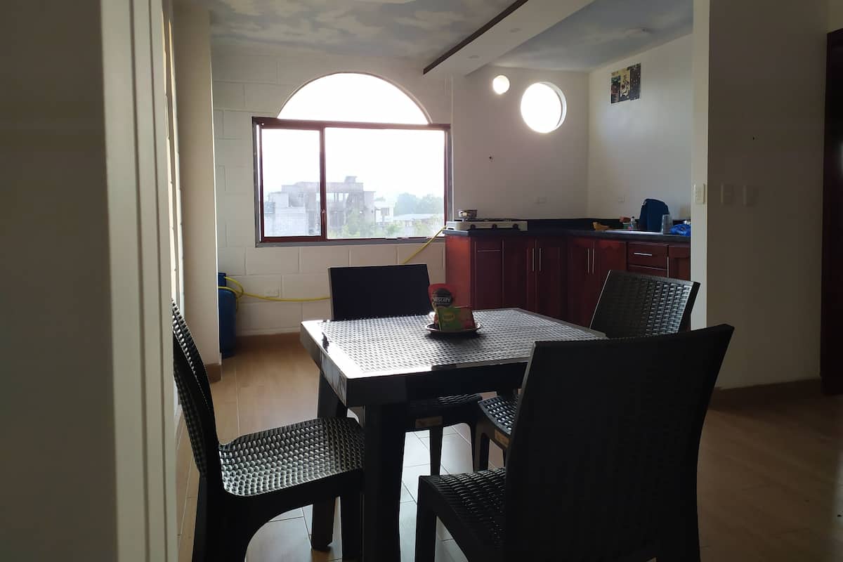 Un comedor con mesa y sillas, una ventana con vistas a edificios, y una zona de cocina con armarios y estufa.