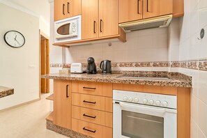 A kitchen with wooden cabinets, a microwave, a coffee maker, a toaster, and an oven.