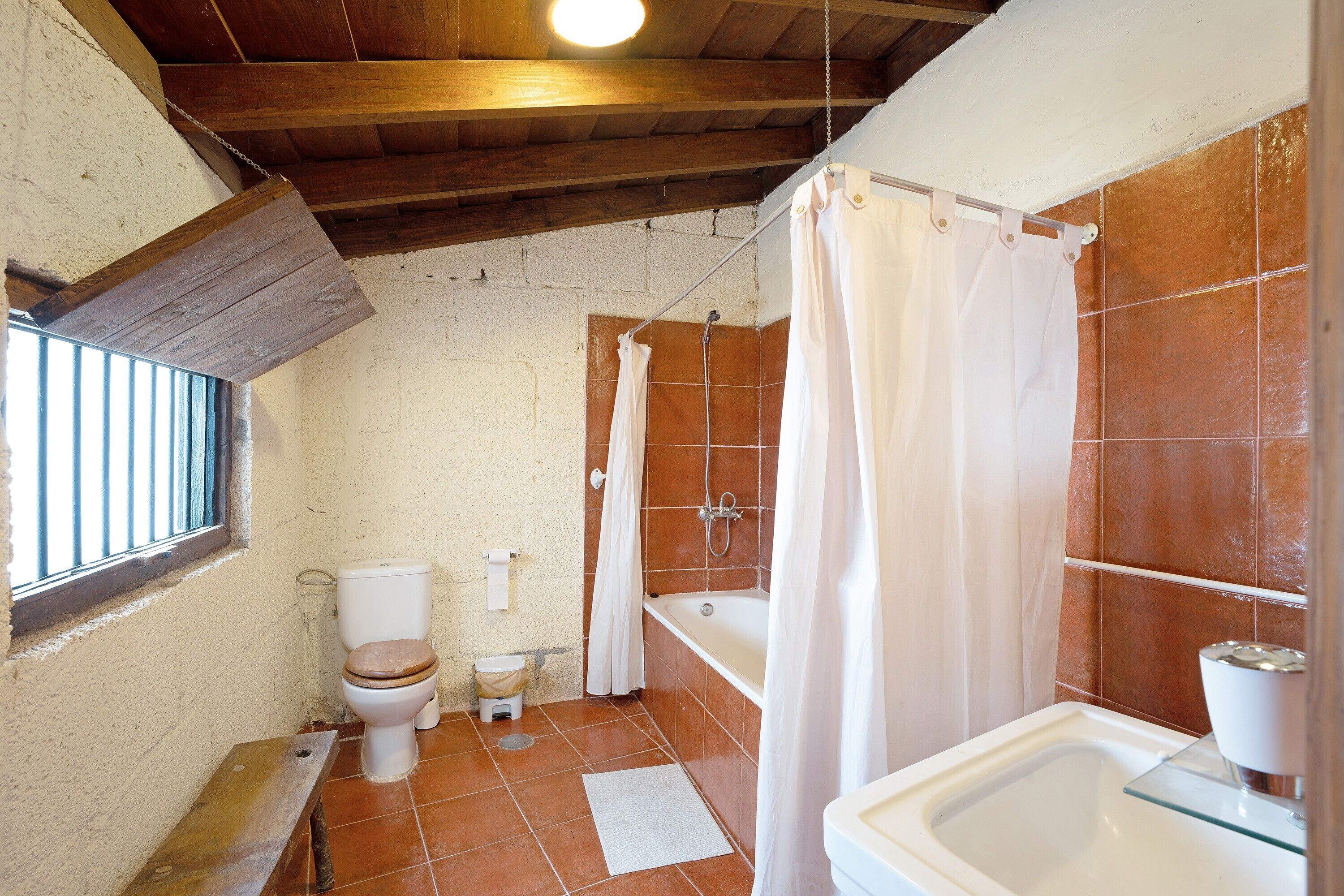 A bathroom with a wooden ceiling, a bathtub, a toilet, and a shower curtain.
