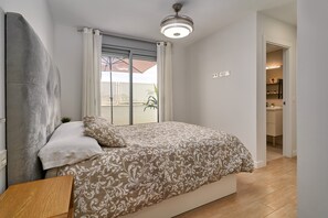 Une chambre à coucher comprenant un lit, une table de chevet, un ventilateur de plafond, une fenêtre avec des rideaux et une vue sur l’extérieur.
