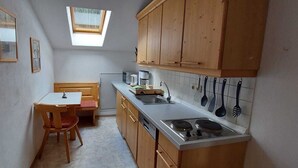 Eine kompakte Küche mit Holzschränken, einem Esstisch, einem kleinen Fenster und einem eingebauten Geschirrspüler.