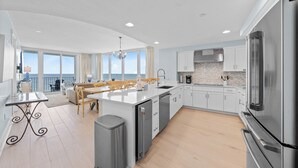 Une cuisine moderne dotée d’un grand îlot central, d’appareils électroménagers en acier inoxydable et offrant une vue sur l’extérieur.