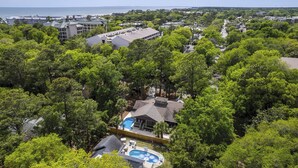 Zona residencial con una casa grande que tiene piscina, rodeada de abundante vegetación y vistas al mar.