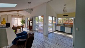 A spacious living area with a high ceiling, a dining area with a table and chairs, a kitchen with a window, and a sliding glass door leading to an outdoor patio. - Beautiful architect-designed villa 30 m from the beach ☀️ (Andernos-les-Bains)