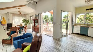 A spacious living area with a sofa, a dining table, and a kitchen area with a view to the outside. - Beautiful architect-designed villa 30 m from the beach ☀️ (Andernos-les-Bains)
