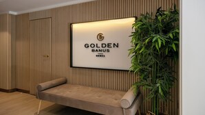 A reception area with a framed sign reading "GOLDEN BANUS HOMES," a cushioned bench, vertical wooden paneling, and a potted plant. - RDR254 - Stunning 1 bedroom Apt. Golden Banús! (Marbella)