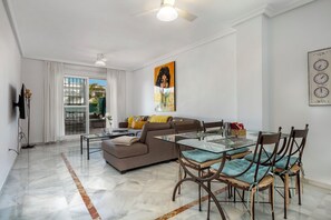 A modern living room with a glass dining table, brown sofa, and a large painting on the wall.