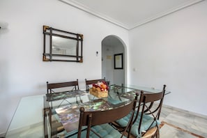 A dining area with a glass table, cushioned chairs, and a wicker basket with fruits.
