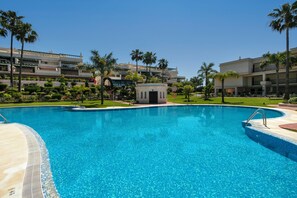 A swimming pool with a clear blue water, surrounded by palm trees and a building with a modern design.