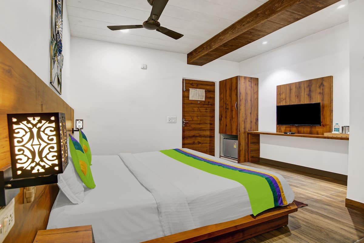 Une chambre à coucher comprenant un lit, une tête de lit en bois, un ventilateur de plafond, une télévision et une petite kitchenette.