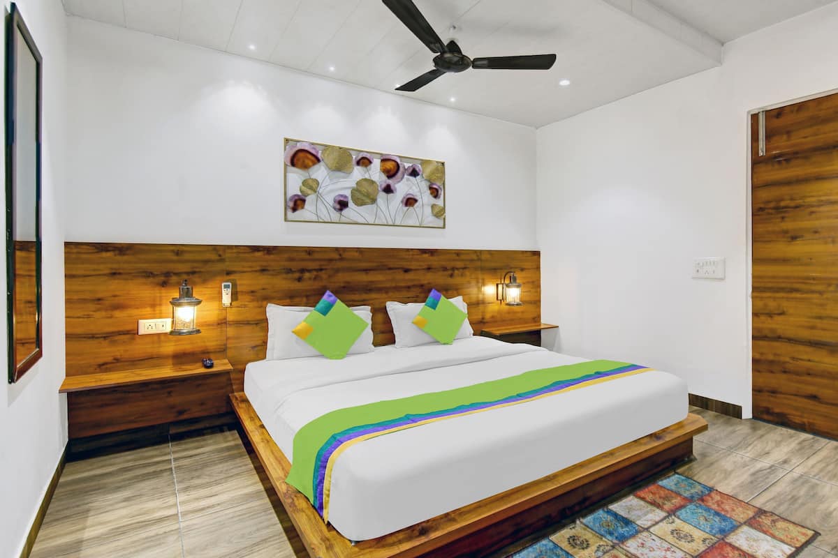 Une chambre à coucher bien aménagée, avec une tête de lit en bois, un ventilateur de plafond, une œuvre d’art accrochée au mur et une table de chevet avec une lampe.