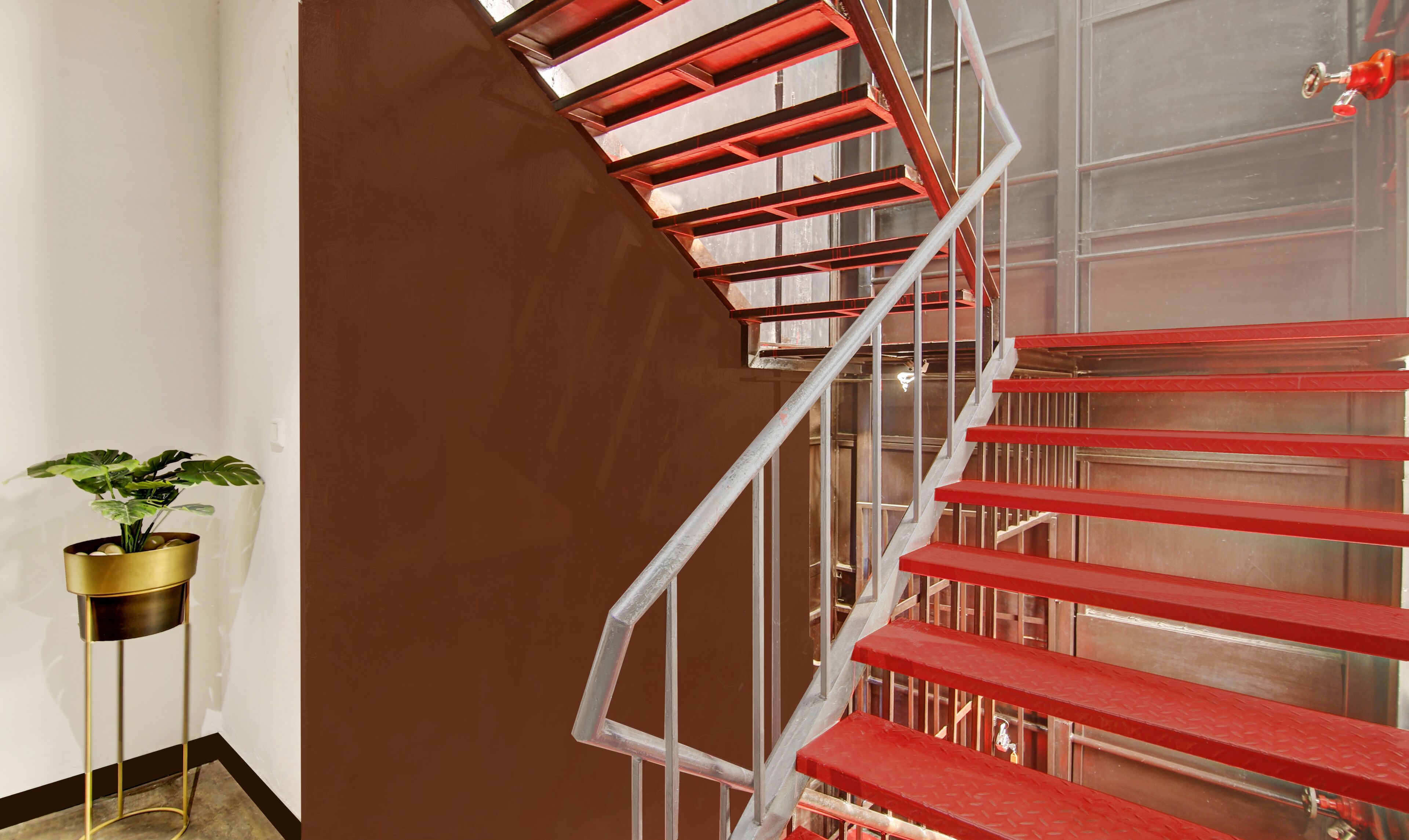 Una escalera con escalones rojos y barandillas de metal, una planta en maceta y una pared marrón.