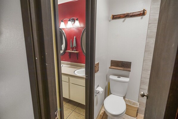 A bathroom with a white toilet, a red wall, and a mirror with lights.