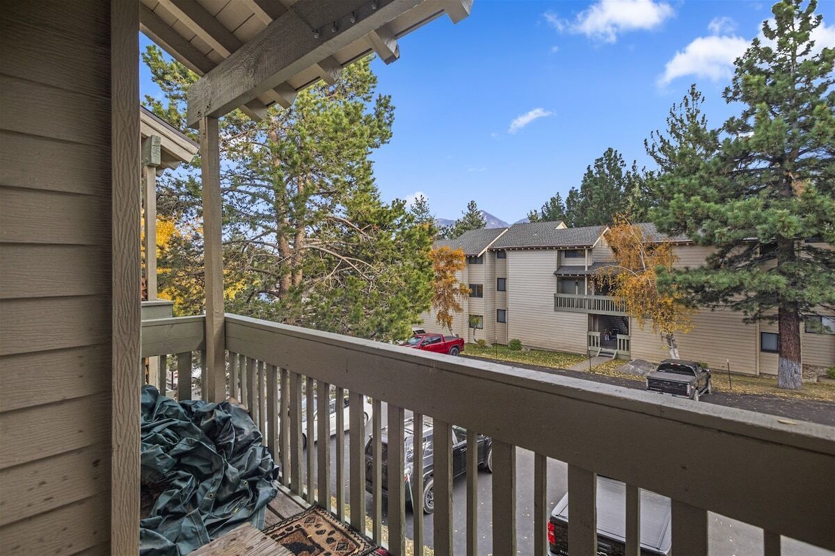 A residential area with a wooden deck, a covered porch, and a view of apartment buildings and trees.