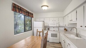 A small kitchen with white cabinets, a wooden table, and a window with curtains.