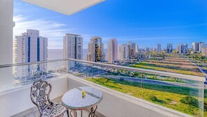 A balcony with a glass railing, a round table, and a chair, overlooking a cityscape with high-rise buildings and a green park. - Wood Summer 2B W/Parking, Wifi & View. (Viña del Mar)