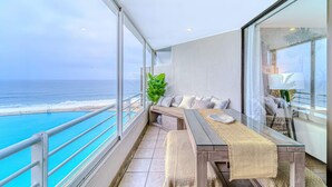 A balcony with a view of the ocean, a seating area with cushions, and a table with a woven placemat. - Bay Dream 2B W/Wifi, Grill & View. (Algarrobo)