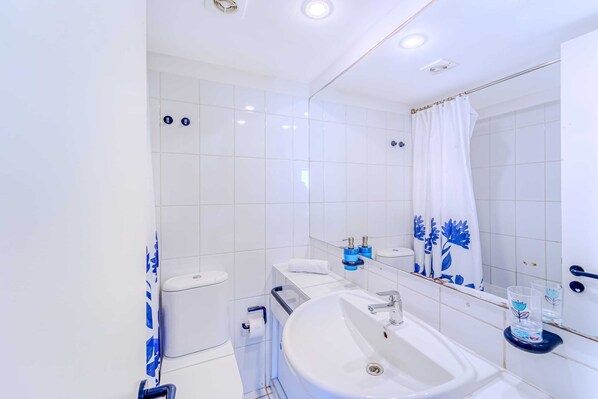 A modern bathroom with white tiles, a sink, a toilet, and a shower curtain. - Bay Dream 2B W/Wifi, Grill & View. (Algarrobo)