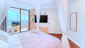 A bedroom with a large bed, a TV, a sliding glass door to a balcony, and a small kitchenette. - Bay Dream 2B W/Wifi, Grill & View. (Algarrobo)