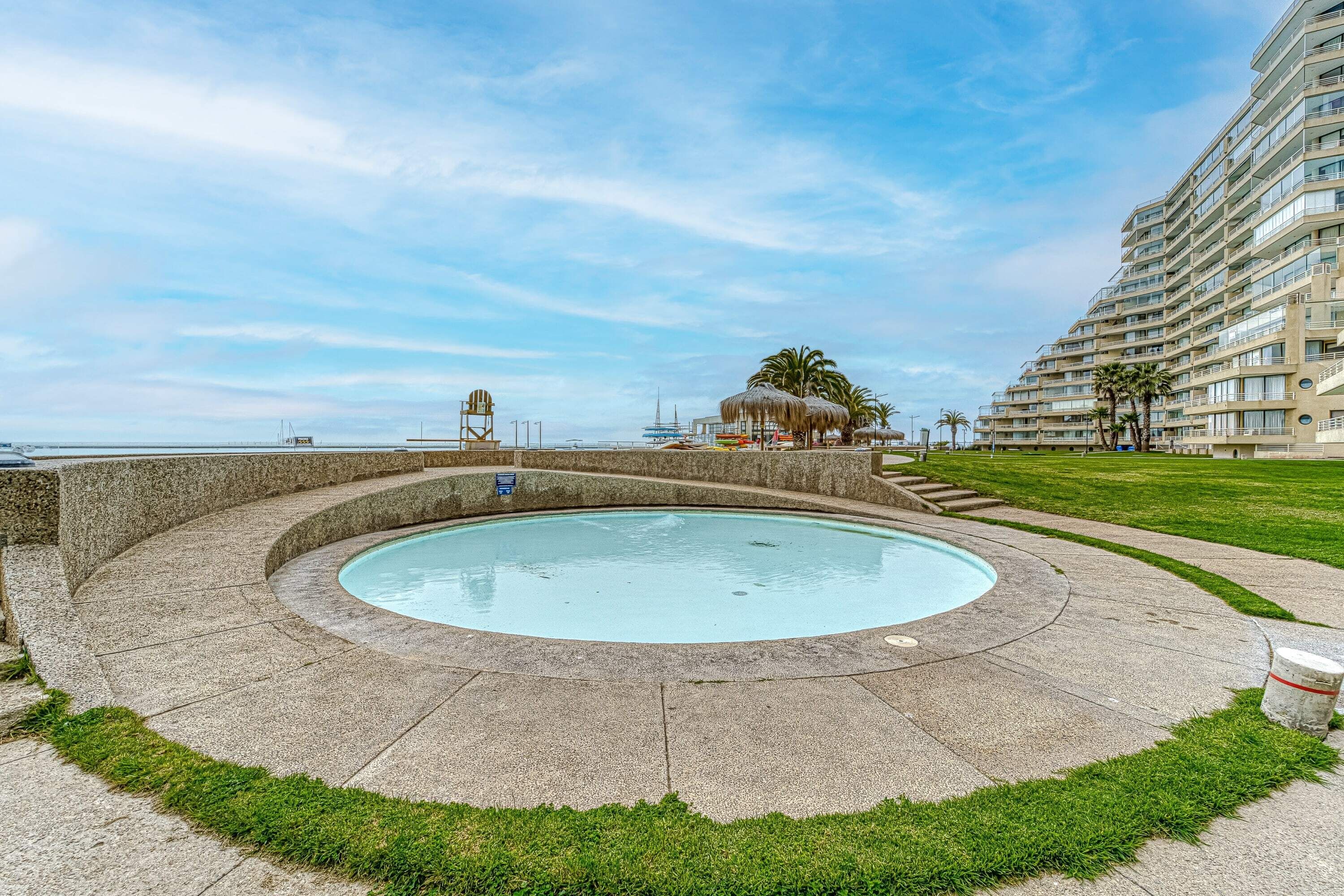 A pool with a circular design, surrounded by a stone deck and grass.