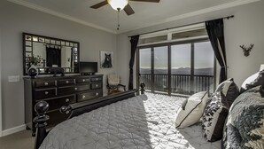 A bedroom with a large bed, a dresser, a ceiling fan, a TV, a window with a view, and a deer head decoration. - Unbeatable views at 5,200 ft and walking distance to slopes. (Sugar Mountain)
